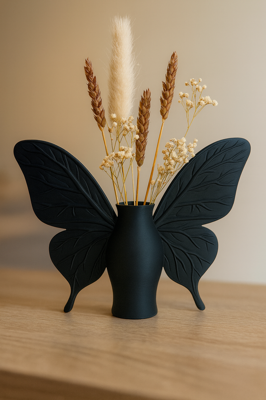 „Mattschwarze Vase mit Schmetterlingsflügeln, 18 cm hoch, 20 cm breit, Öffnung 30 mm, bestückt mit Trockenblumen.“
